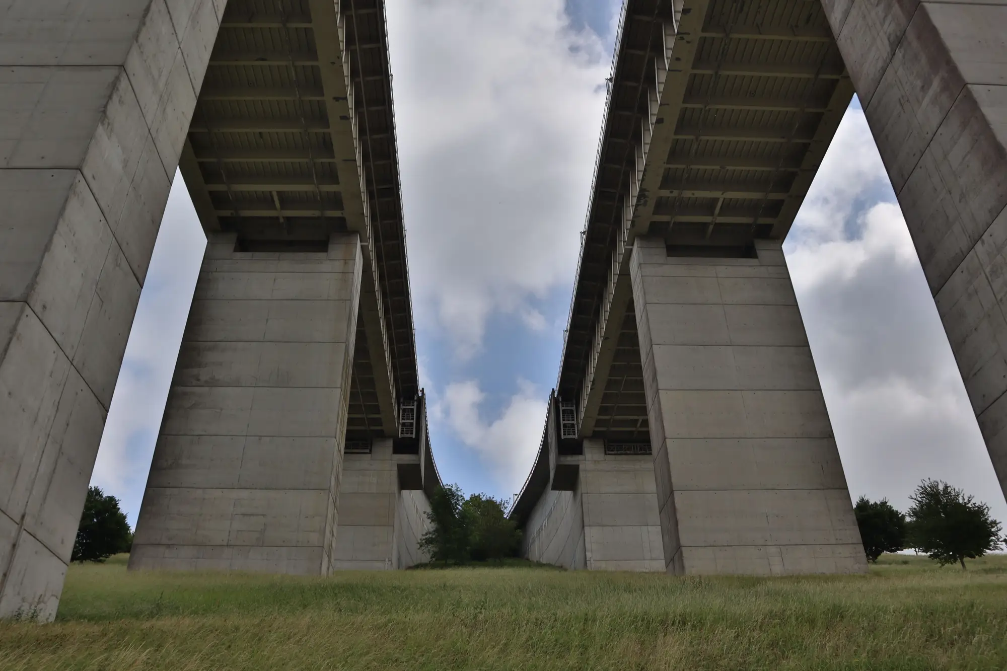 Two concrete viaduct decks seen from the ground between their tall piers